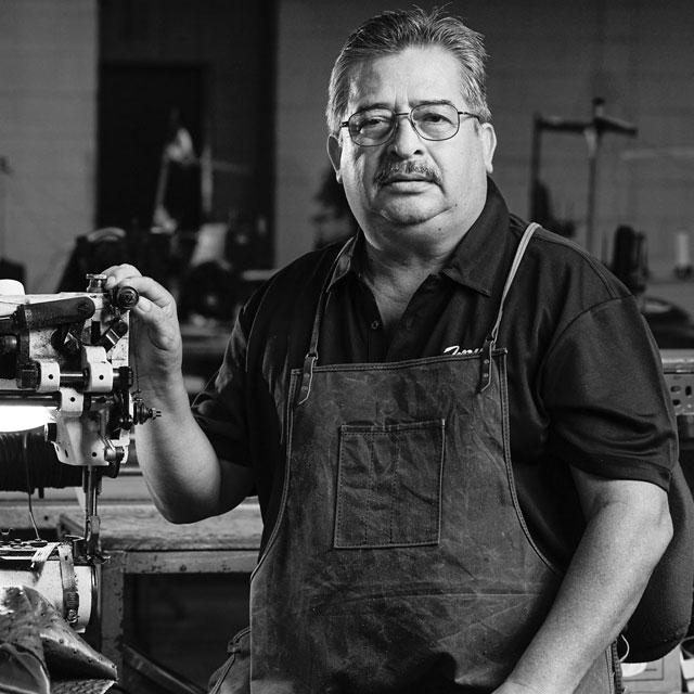 A Hispanic man wearing a polo shirt and an apron looks into the camera.